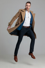 young smartcasual guy in longcoat jumping in the air