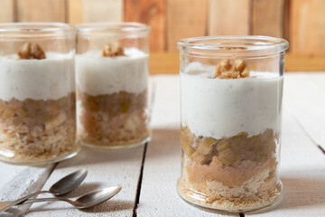süßer gekochter zubereiteter Rhabarber im Glas unter Quark und Joghurt mit Walnüssen und Biscuit auf Tisch aus Holz in der Küche