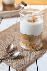 süßer gekochter zubereiteter Rhabarber im Glas unter Quark und Joghurt mit Walnüssen und Biscuit auf Tisch aus Holz in der Küche