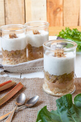 süßer gekochter zubereiteter Rhabarber im Glas unter Quark und Joghurt mit Walnüssen und Biscuit auf Tisch aus Holz in der Küche
