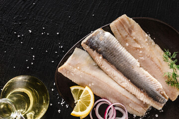 Marinated fillet mackerel or fillet herring fish with spices, greens and slice of bread on plate over dark stone background. Mediterranean food, appetizer, seafood, top view - obrazy, fototapety, plakaty