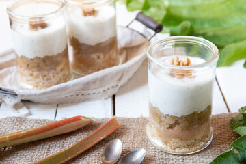 süßer gekochter zubereiteter Rhabarber im Glas unter Quark und Joghurt mit Walnüssen und Biscuit auf Tisch aus Holz in der Küche