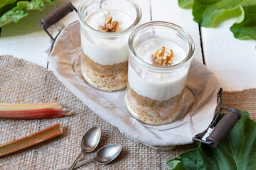 süßer gekochter zubereiteter Rhabarber im Glas unter Quark und Joghurt mit Walnüssen und Biscuit auf Tisch aus Holz in der Küche