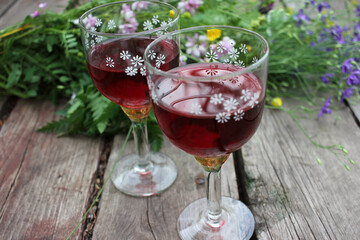 Midsummer night's dream strawberry elderflower cocktail, and wild blue and yellow flowers on the wooden board background. Two glasses of red wine with berries. Selective focus. Copy space
