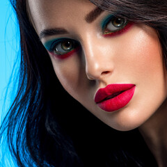 Portrait of beautiful young woman with bright blue makeup. Beautiful brunette with bright red...