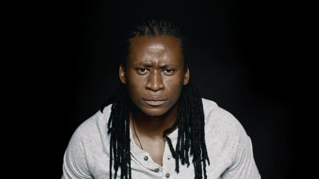 African male with dreadlocks looking angry on black background. Man staring at camera with serious expression.
