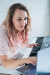 A friendly woman plays the electronic piano and conducts a video blog on her laptop. Stay home. Musical instrument teacher. Distance learning music quarantined.