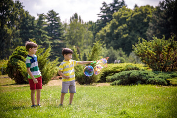 Obraz premium Boy blowing soap bubbles while an excited kid enjoys the bubbles. Happy teenage boy and his brother in a park enjoying making soap bubbles. Happy childhood friendship concept