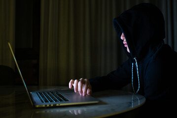Hacker is  hacking into the computer network. Young boy in a dark room with laptop.  Hacker with a laptop.