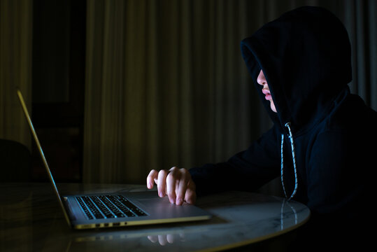 Hacker Is  Hacking Into The Computer Network. Young Boy In A Dark Room With Laptop.  Hacker With A Laptop.