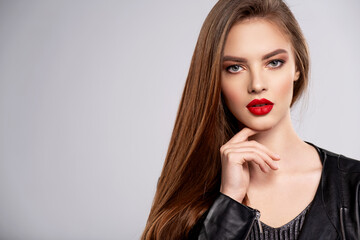 Portrait of beautiful young woman with bright makeup. Beautiful brunette with bright red lipstick on her lips. Pretty girl with long brown hair. Brunette dressed in a black leather jacket. Sexy girl