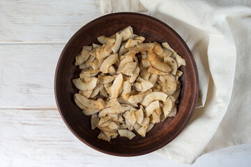 Delicious crispy coconut chips with salted caramel in a brown ceramic plate. Natural product made from coconut pulp. Useful snack for a snack. The concept of proper nutrition.