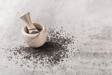 Black sesame crushed font view arrangement in pestle on gray rustic concrete like background studio shot