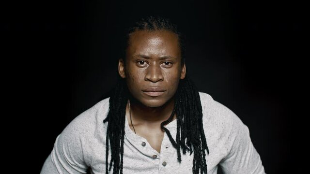 African male with dreadlocks on black background. Muscular man looking at camera.
