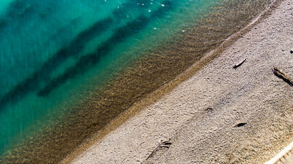 The expanse of the sea meets the sandy beach. Soft sea waves of blue transparent water on the beach. A soft wave of blue tropical beach serenity, a natural backdrop for summer holidays. Aerial view fr