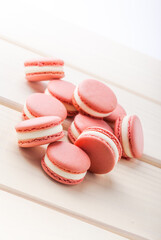 Pink raspberry macaroons with white chocolate filling fresh close-up slanted arrangement on white wooden table selective focus studio shot