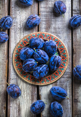 Plums arrangement on colorful plate overhead on old wooden table
