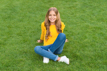 Fototapeta premium happy little girl has long curly hair. kid beauty and fashion. teen girl after hairdresser. relax on green grass. spring leisure time. happy childhood. kid with stylish hair. cheerful smile