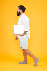 In trendy hipster style. Hipster hold computer yellow backgrounf. Bearded man with hipster beard in casual style. Hipster fashion. Modern life. Using new computing technologies