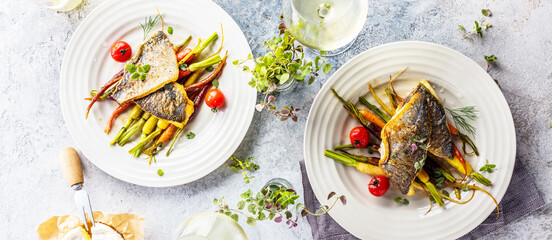 top view of delicious fish with vegetables on white plates and wine glasses on grey surface
