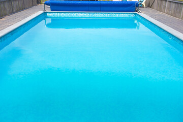Modern swimming pool with pool cover for protection dirt rolled up and pool ladder in garden.