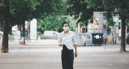 The image face of a Business Asian man wearing a doctor mask to prevent germs, toxic fumes, and COVID 19, He is reading and listening to the news on tablets and newspapers, do not work in the park.