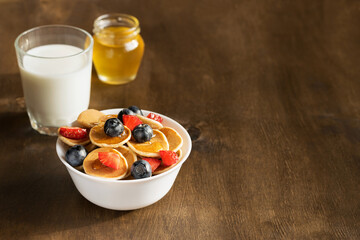 Mini pancakes with strawberries and blueberries in a white bowl. Delicious breakfast.