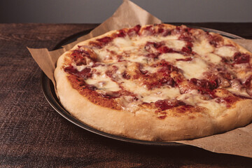 Homemade pizza with mozzarella and ham with basil. On a wooden table top.