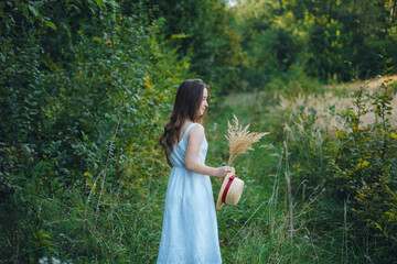 Beautiful girl in a white dress with a bouquet of dried flowers. Young woman in a green park. Girl...