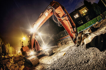 Orange excavator digger working at night on the street
