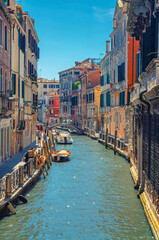 Fototapeta na wymiar Venice cityscape with narrow water canal with moored boats between old colorful multicolored buildings and stone promenade, Veneto Region, Northern Italy. vertical view, blue sky background.