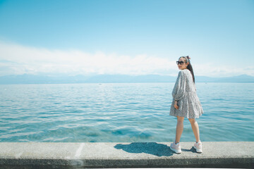 Beautiful Asian woman with white skin and long black hair Wearing black glasses. feeling happy to Sit on stone and watching the lake view On a clear sky day, Tourism and summer vacations.