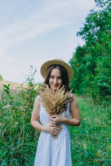 Beautiful girl in a white dress with a bouquet of dried flowers. Young woman in a green park. Girl in a dress and a summer sunny day.