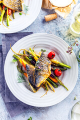 top view of delicious fish with vegetables on white plates and wine glasses on grey surface