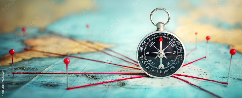Poster magnetic compass and location marking with a pin on routes on world map. adventure, discovery, navig