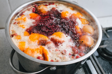 Fresh fruits are boiled in boiling water in a metal pan on the stove. Delicious stewed apricot, apples, cherries, raspberries. Photography, concept.