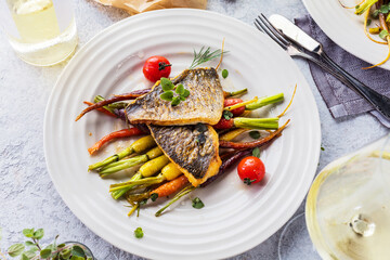 top view of delicious fish with vegetables on white plates and wine glasses on grey surface