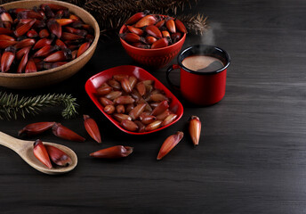 Typical araucaria seeds used as a condiment in Brazilian cuisine in winter. Brazilian pine in red brown wooden bowl with coffee cup on gray background