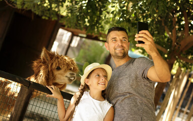 Selfie time! Family and holiday concept. Cute father with daughter feeding  their  friend lama, smiling and have fun in the zoo. Cool weekend