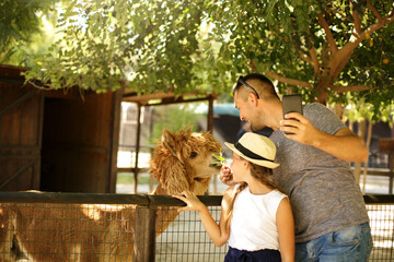 Selfie time! Family and holiday concept. Cute father with daughter feeding  their  friend lama,...