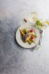 top view of delicious fish with vegetables on white plates and wine glasses on grey surface