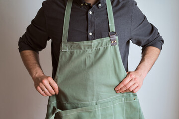 A man in a kitchen apron. Chef work in the cuisine. Cook in uniform, protection apparel. Job in food service. Professional culinary. Green fabric apron, casual stylish clothing. Handsome baker posing