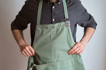 Foto op Canvas A man in a kitchen apron. Chef work in the cuisine. Cook in uniform, protection apparel. Job in food service. Professional culinary. Green fabric apron, casual stylish clothing. Handsome baker posing © Iuliia Pilipeichenko