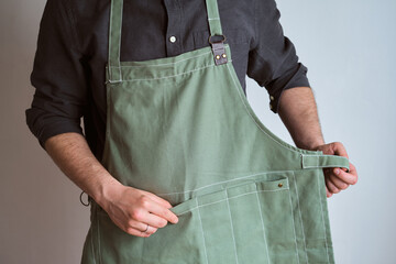 A man in a kitchen apron. Chef work in the cuisine. Cook in uniform, protection apparel. Job in food service. Professional culinary. Green fabric apron, casual stylish clothing. Handsome baker posing