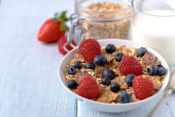 Granola with blueberries and raspberries in white bowl on dark white desk.