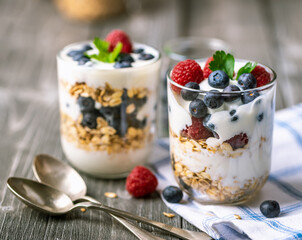 White yogurt in glass jar with fruits on grey background.