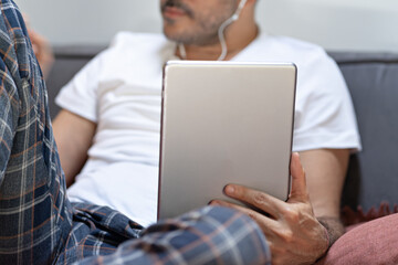 man holding using digital tablet and headphones in bed at home with pijama. Online education, working, video call