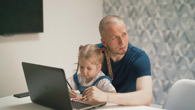 concept of: little daughter sits on her dad's lap writes in notebook, listens to teacher from laptop, is on distance learning, father misses, dreamily looks out window, helps