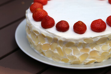 Fresh and delicious homemade summertime theme strawberry, almond and cream cake. Topped with whipped cream, fresh berries and almond slices. Cheerful closeup color portrait image of the cake.