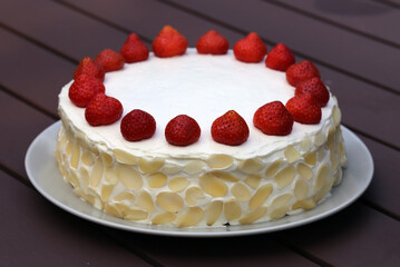 Fresh and delicious homemade summertime theme strawberry, almond and cream cake. Topped with whipped cream, fresh berries and almond slices. Cheerful closeup color portrait image of the cake.